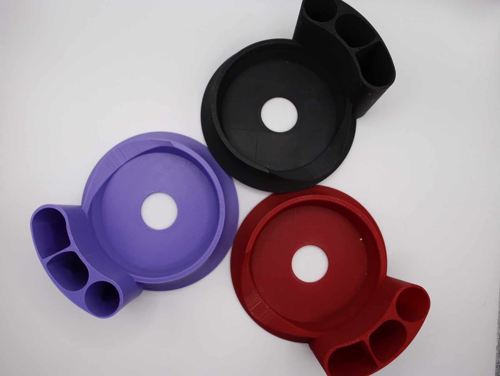 Top view of purple, red, and black Peak Pro stands showing one round slot and two larger storage slots.